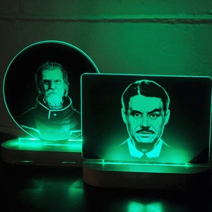 Op de afbeelding: Twee verlichte acrylportretten op houten bases. De portretten zijn van mannen met gezichtshaar. De portretten worden van onderen verlicht met groen licht.