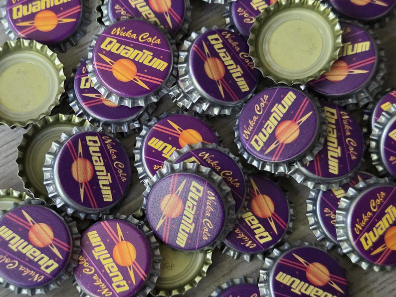 May include: A collection of metal bottle caps featuring a purple background with a yellow planet graphic and the text Nuka Cola Quantum. The caps have a serrated edge and some are flipped over to show the plain metallic interior lining.