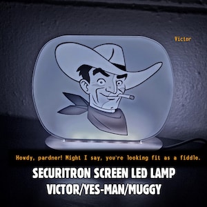 May include: An oval-shaped LED lamp featuring a graphic of a cowboy with a cigarette. The text Victor appears in the top right. Below the lamp, the text reads: Howdy, pardner! Might I say, you're looking fit as a fiddle. SECURITRON SCREEN LED LAMP VICTOR/YES-MAN/MUGGY.