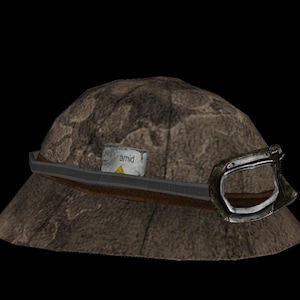 May include: A brown hat with a textured surface, a dark brown band, and a silver buckle. A small, rectangular label with the word "amid" is attached to the hat.