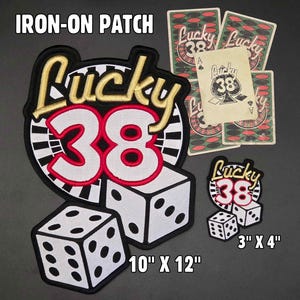 May include: Iron-on patches with a casino theme. The patches feature the text "Lucky 38" in gold and red, dice, and playing cards. The largest patch measures 25.4 cm x 30.5 cm, and a smaller one is 7.6 cm x 10.2 cm.