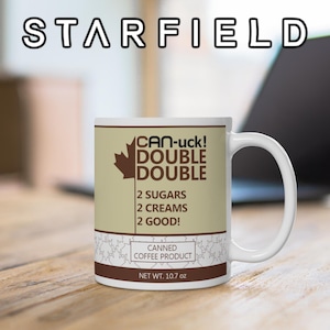 May include: White ceramic mug with the text "STARFIELD" at the top. The mug features the text "CAN-uck! DOUBLE DOUBLE" with a maple leaf graphic, and "2 SUGARS 2 CREAMS 2 GOOD!" The mug is labeled "CANNED COFFEE PRODUCT" and "NET WT. 10.7 oz."