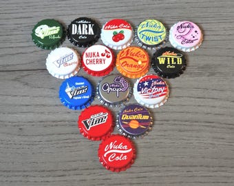 May include: A collection of fourteen metal bottle caps featuring various colorful graphic designs and logos, including Nuka-Cola, Nuka-Cherry, Nuka-Orange, Nuka-Wild, Nuka-Grape, Nuka-Victory, Nuka-Quantum, Nuka-Twist, Nuka-Dark, Vim, and Vim Quartz.