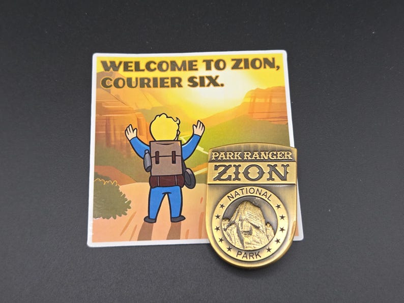 May include: A sticker and a gold-colored metal pin. The sticker reads "WELCOME TO ZION, COURIER SIX." with a cartoon figure. The pin is a Zion National Park Park Ranger badge with a mountain image.