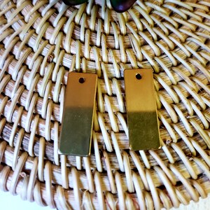 May include: Two gold-colored rectangular metal earrings with a hole at the top.