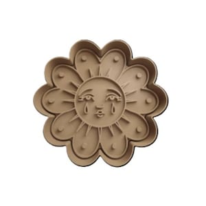 Può includere: Un tagliabiscotti a forma di fiore color beige con un volto di sole piangente al centro. Il tagliabiscotti ha un bordo smerlato ed è realizzato in plastica. Il sole ha gli occhi chiusi e lacrime.