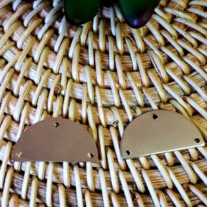 Puede incluir: Dos formas de medio círculo de metal de color dorado con agujeros sobre un fondo de mimbre tejido.