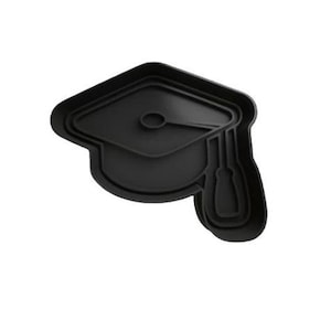 Puede incluir: Cortador de galletas de plástico negro con forma de gorro de graduación. El gorro tiene un borlón y una parte superior cuadrada.