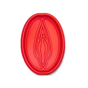 May include: A red, oval-shaped cookie cutter with a detailed interior design. The cutter features a layered, stylized anatomical form. The object is made of plastic and is set against a white background.