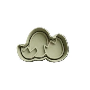 May include: A white plastic cookie cutter shaped like two eggs, one of which is cracked open. The cutter is designed for making cookies or other baked goods.