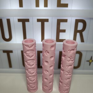 Op de afbeelding: Drie roze deegrollers met verschillende reliëfmotieven. De motieven zijn harten, cirkels en potafdrukken.