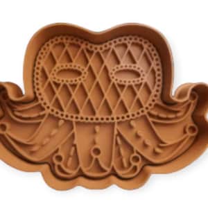 May include: Brown plastic cookie cutter shaped like a jester's mask with a diamond pattern and a crown.
