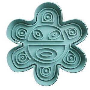 May include: A teal blue cookie cutter shaped like the Taino sun symbol, a stylized face with concentric circles and a flower-like design.