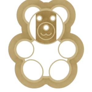 May include: A brown teddy bear cookie cutter with a simple design. The cutter has a round head with two small circles for eyes and a small circle for a nose. The bear has a rounded body with two small circles for paws.