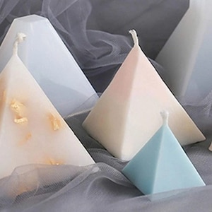 Può includere: Quattro candele a forma di piramide in diversi colori, tra cui bianco, azzurro e rosa. Le candele sono fatte di cera e hanno una finitura liscia e lucida.