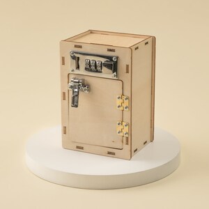 May include: A wooden toy safe with a combination lock and a latch. The safe is painted in a light wood color and has a small door that opens to reveal an empty interior.
