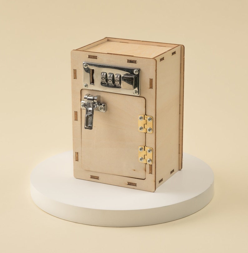May include: A wooden toy safe with a combination lock and a latch. The safe is painted in a light wood color and has a small door that opens to reveal an empty interior.