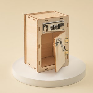 May include: A wooden toy safe with a combination lock and a hinged door that is open. The safe is made of light wood and has a natural finish.