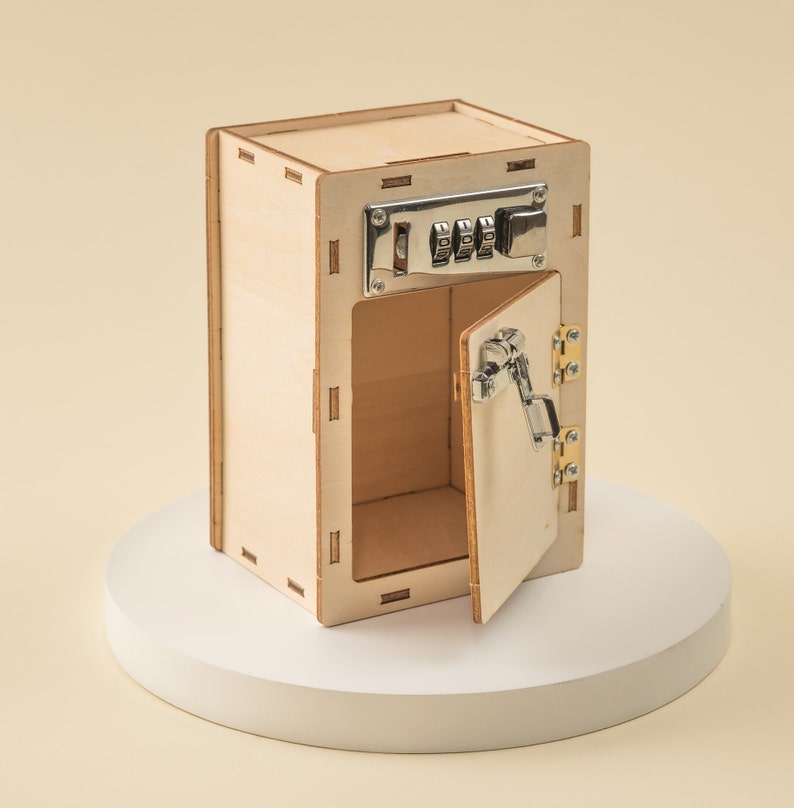 May include: A wooden toy safe with a combination lock and a hinged door that is open. The safe is made of light wood and has a natural finish.