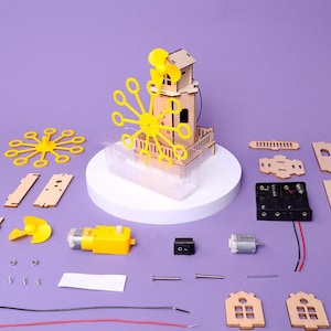 May include: A disassembled wooden windmill kit with various components, including a yellow fan, motor, and switch. The kit features a small wooden house structure and a clear plastic container, all arranged on a purple surface.
