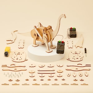 Puede incluir: Un kit de juguete de dinosaurio de madera con control remoto. El kit incluye una variedad de piezas, incluyendo el cuerpo del dinosaurio, las patas, la cola y la cabeza. El dinosaurio est&aacute; ensamblado sobre una base blanca. El kit tambi&eacute;n incluye un destornillador y una peque&ntilde;a herramienta amarilla.