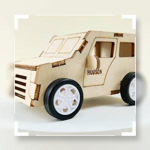 May include: A wooden toy car with black tires and white wheels. The car has a door with the name "HUDSON" written on it.