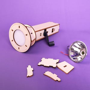 May include: A wooden flashlight kit with a crank handle, a silver reflector, and several wooden pieces. The flashlight is disassembled and ready to be assembled.