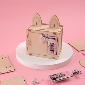 K&ouml;nnte beinhalten: Eine Holzkiste mit Zahlenschloss und Hasenohren-Akzenten. Die Kiste ist aus hellem Holz gefertigt und hat ein silbernes Zahlenschloss auf der Vorderseite. Zus&auml;tzliche Holzteile und Hardware sind auf einem rosa Hintergrund verstreut.