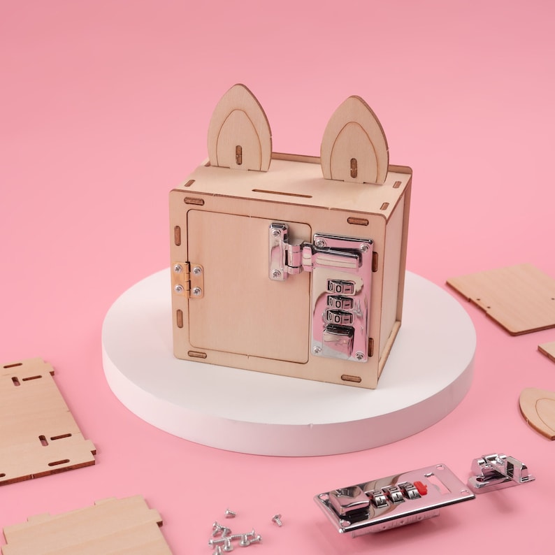 K&ouml;nnte beinhalten: Eine Holzkiste mit Zahlenschloss und Hasenohren-Akzenten. Die Kiste ist aus hellem Holz gefertigt und hat ein silbernes Zahlenschloss auf der Vorderseite. Zus&auml;tzliche Holzteile und Hardware sind auf einem rosa Hintergrund verstreut.