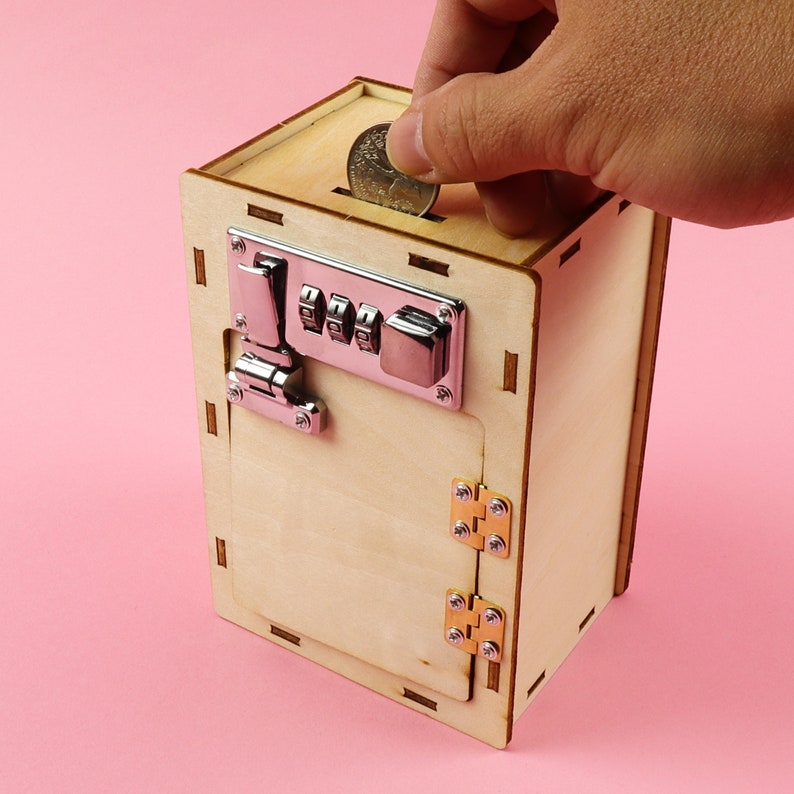 May include: A wooden toy safe with a combination lock, hinges, and a slot for inserting coins. The safe is painted brown and has a light wood grain texture.
