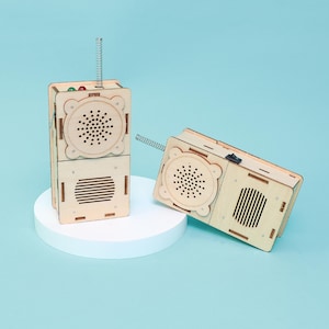 May include: Two wooden toy radios with a light wood finish. One radio is stacked on top of another, and the other is lying on its side. Each has a speaker, a spring antenna, and a switch.