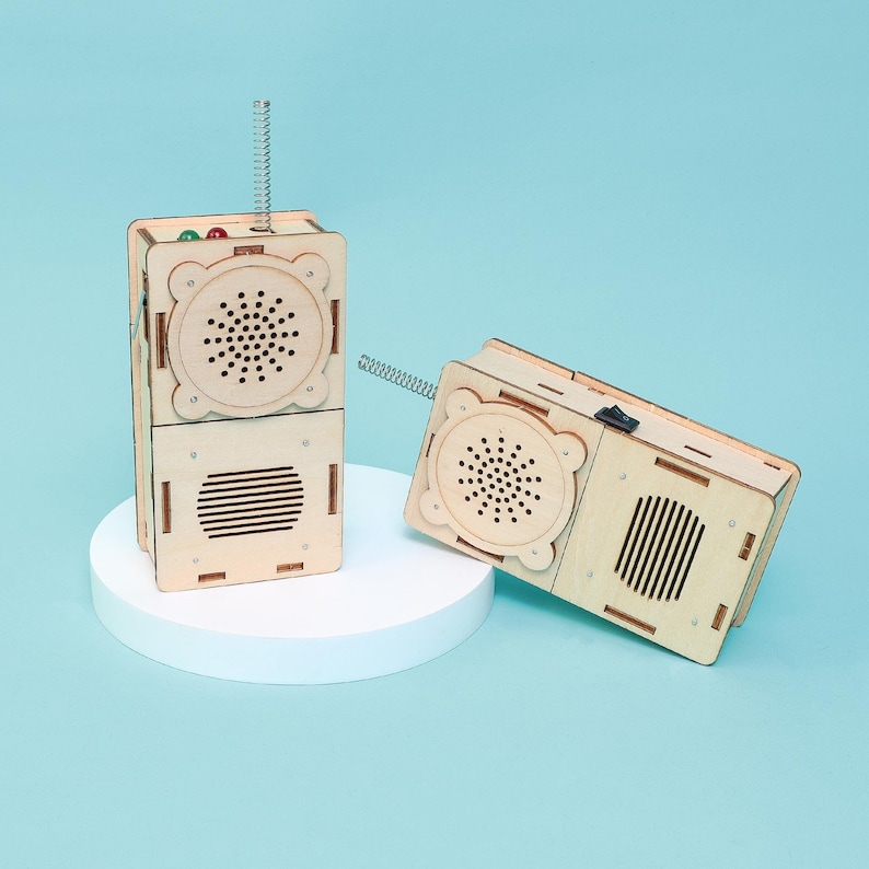 May include: Two wooden toy radios with a light wood finish. One radio is stacked on top of another, and the other is lying on its side. Each has a speaker, a spring antenna, and a switch.