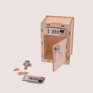 May include: A wooden toy safe with a combination lock, a latch, and a hinged door. The safe is open and the door is partially open. The safe is made of light wood and has a natural finish. The combination lock is silver and has three dials. The latch is silver and has a lever handle. The hinges are brass and are attached to the door and the safe. The safe is sitting on a white surface.