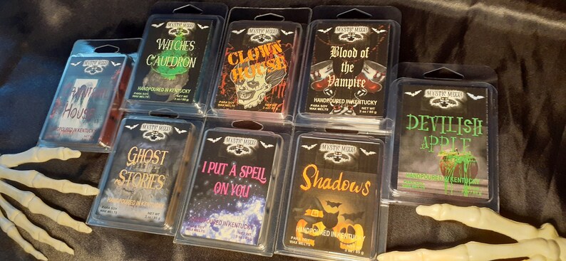 May include: A collection of Halloween-themed wax melts in clear plastic packaging. Each melt features a unique design and spooky name, including "Witches Cauldron," "Clown House," and "Blood of the Vampire." The packaging includes the brand name "Mystic Mood."