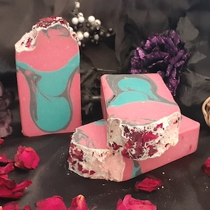 May include: Three bars of handmade soap with pink and teal marbling. The soap is decorated with dried rose petals.