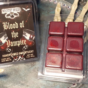 May include: A clear plastic container with six red wax melt cubes and a label that reads "Blood of the Vampire." The label is black with red and white text and features a bat and two goblets. The wax melts are 3 oz / 85 g.