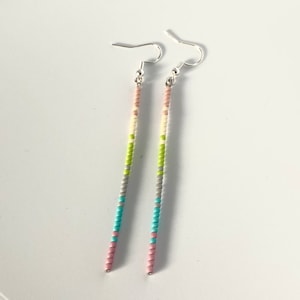 May include: A pair of long, beaded earrings with a silver hook. The beads are in a rainbow pattern of pink, blue, gray, green, and white.