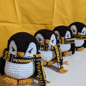 May include: Five black and white crocheted penguin plushies with yellow and black scarves. The scarves have the text "1967 Penguins" and "Penguins" on them.