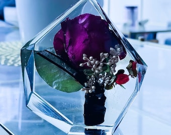 Peut inclure: Un bloc de résine géométrique transparent contenant une rose violette profonde préservée, une feuille verte, de petites brindilles décoratives argentées et une petite baie rouge. La tige de la rose est enveloppée d'un ruban noir, le tout inclus.