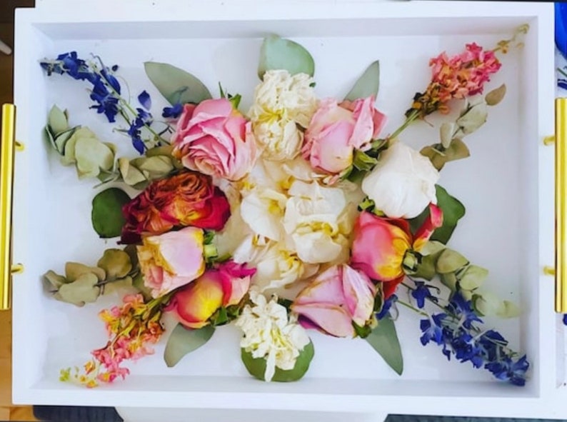 May include: A white tray with a pressed flower arrangement. The arrangement features pink, white, and red roses, white carnations, and blue delphiniums.