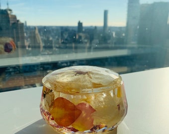 May include: A clear glass trinket box with a faceted design, filled with dried flower petals in shades of pink and yellow.