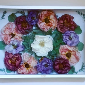 May include: A white tray with a glass insert filled with pressed flowers. The flowers are in shades of pink, purple, and white. The tray has a gold trim.