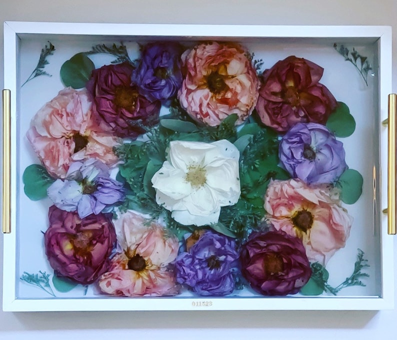 May include: A white tray with a glass insert filled with pressed flowers. The flowers are in shades of pink, purple, and white. The tray has a gold trim.