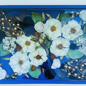 May include: A blue tray with a gold frame, filled with dried white flowers, gold berries, and blue and black stones.