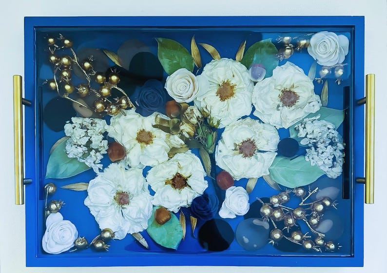 May include: A blue tray with a gold frame, filled with dried white flowers, gold berries, and blue and black stones.