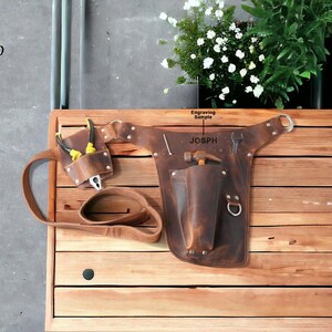 Op de afbeelding: Bruine leren gereedschapsriem met een hamer, schroevendraaier en tang. De riem heeft een band en is gegraveerd met de naam "JOSPH".