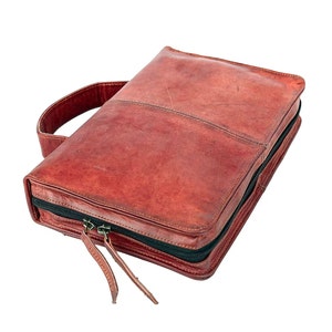 May include: A brown leather zippered travel case with a top handle. The case has a zippered closure and a black zipper pull.