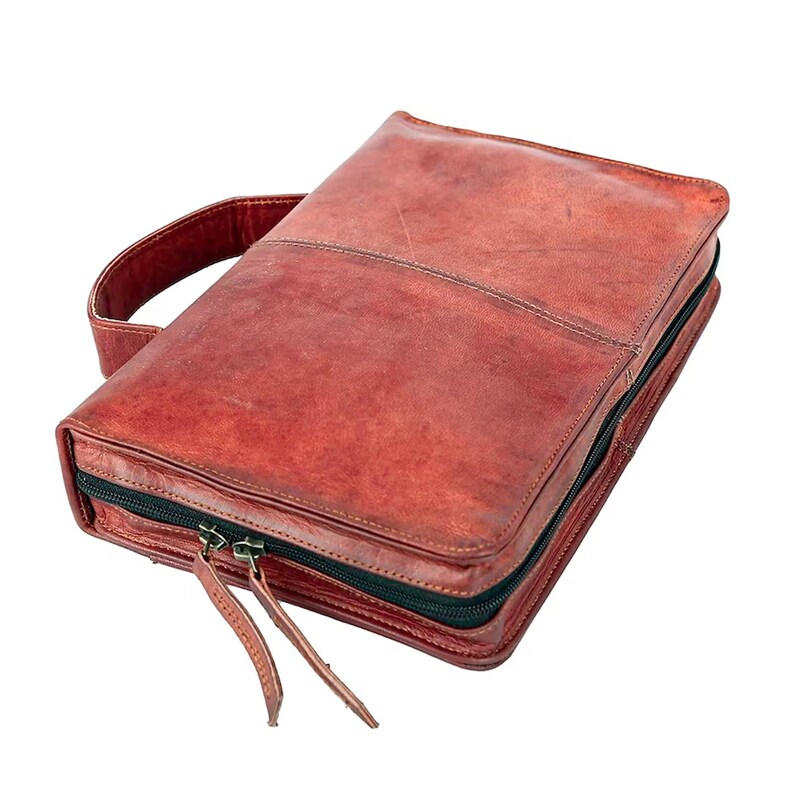 May include: A brown leather zippered travel case with a top handle. The case has a zippered closure and a black zipper pull.