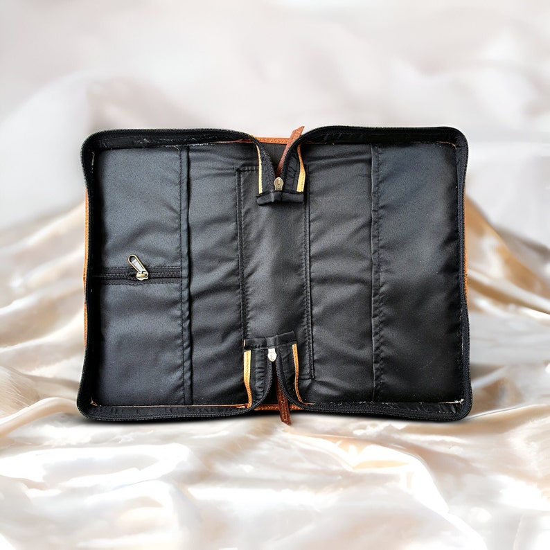 May include: Open brown leather bible cover with black interior and multiple pockets. The cover has a zipper closure and a gold zipper pull.