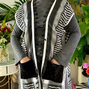 May include: A long, open-front garment with a black, white, and gray geometric pattern. The garment has black velvet pockets and white trim. The sleeves are gray, and the overall style is reminiscent of a traditional Middle Eastern design.
